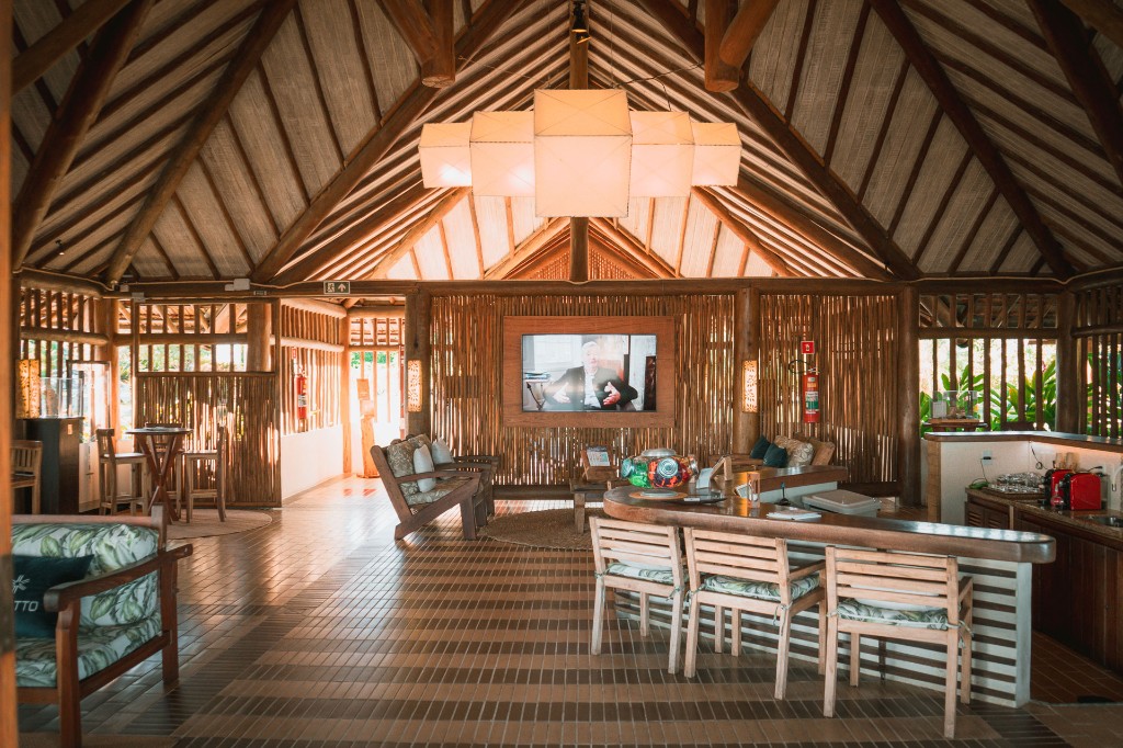 Lounge com tecto em madeira e palha, bar curvo e iluminação de destaque.